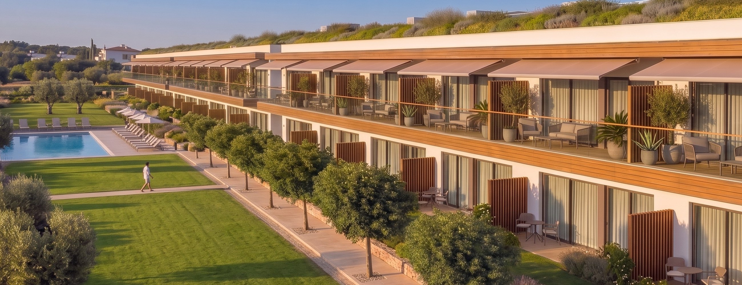Apartmenthaus mit Terrassen und Markisen, offene Rasenfläche bis zum Gemeinschaftspool | Apartment building with terraces and awnings, open lawn running to the communal pool