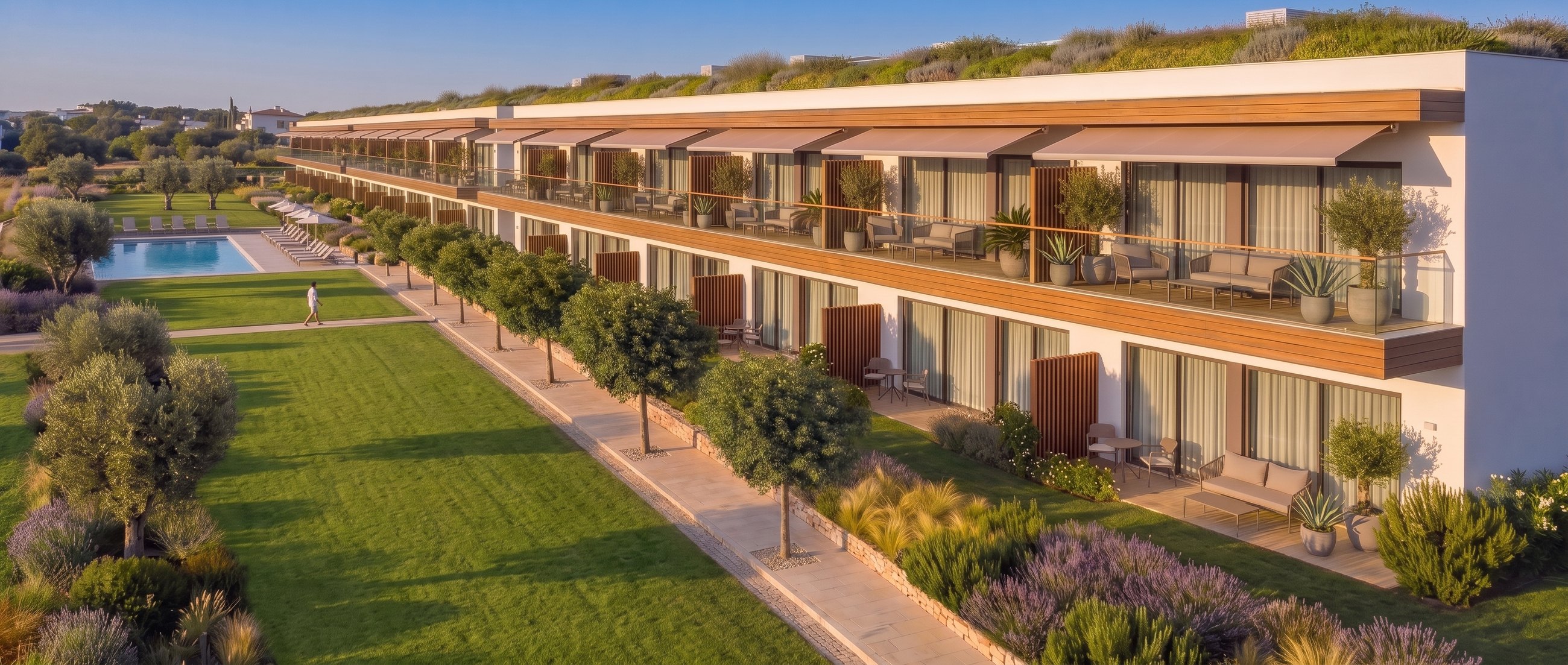 Apartmenthaus mit Terrassen und Markisen, offene Rasenfläche bis zum Gemeinschaftspool | Apartment building with terraces and awnings, open lawn running to the communal pool